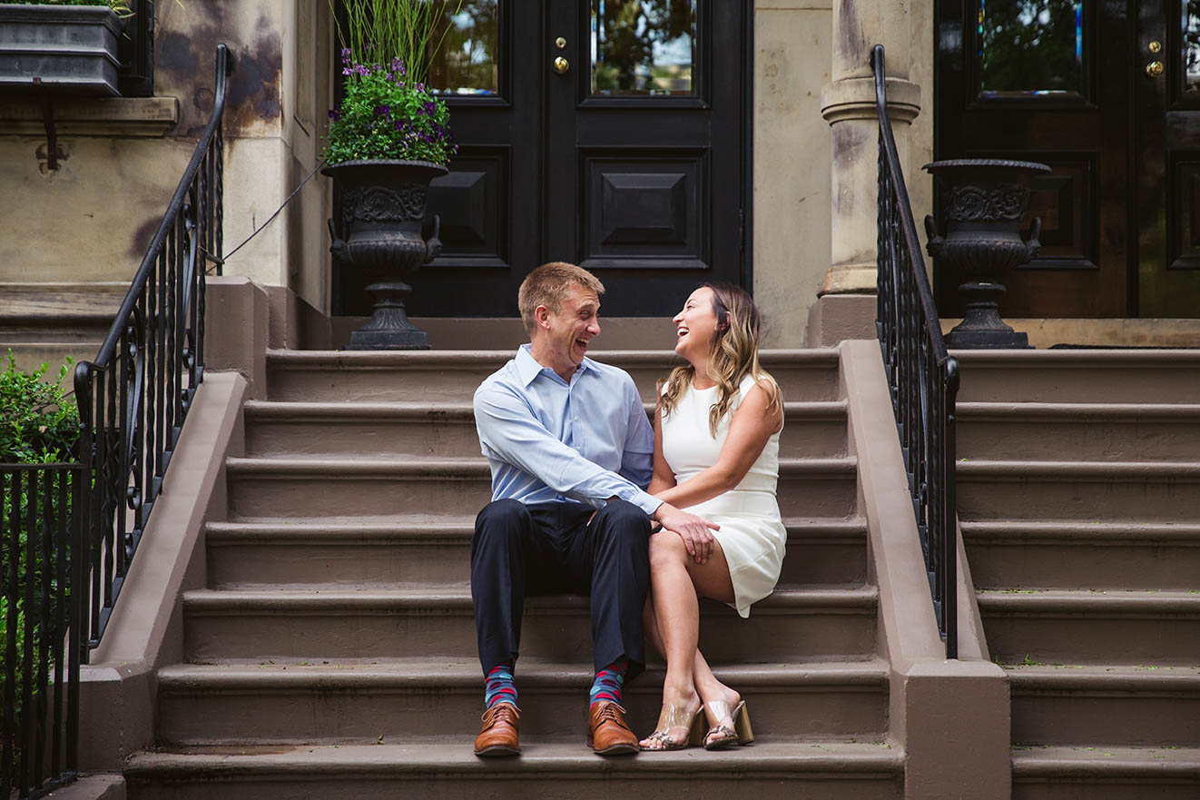 A documentary portrait of a couple laughing together on the front steps of their Back Bay home during their Boston engagement session