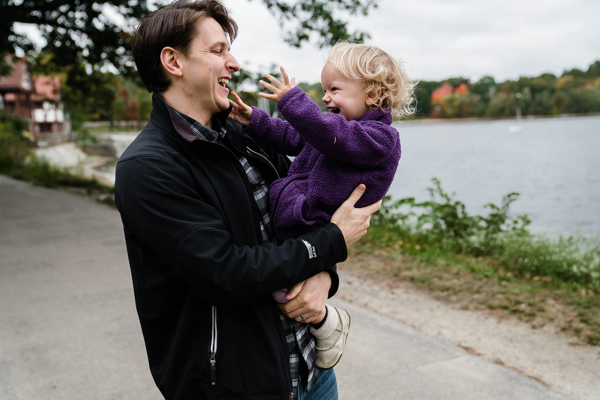 A documentary photograph of a father playing with his daughter during their family session at Jamaica Pond.