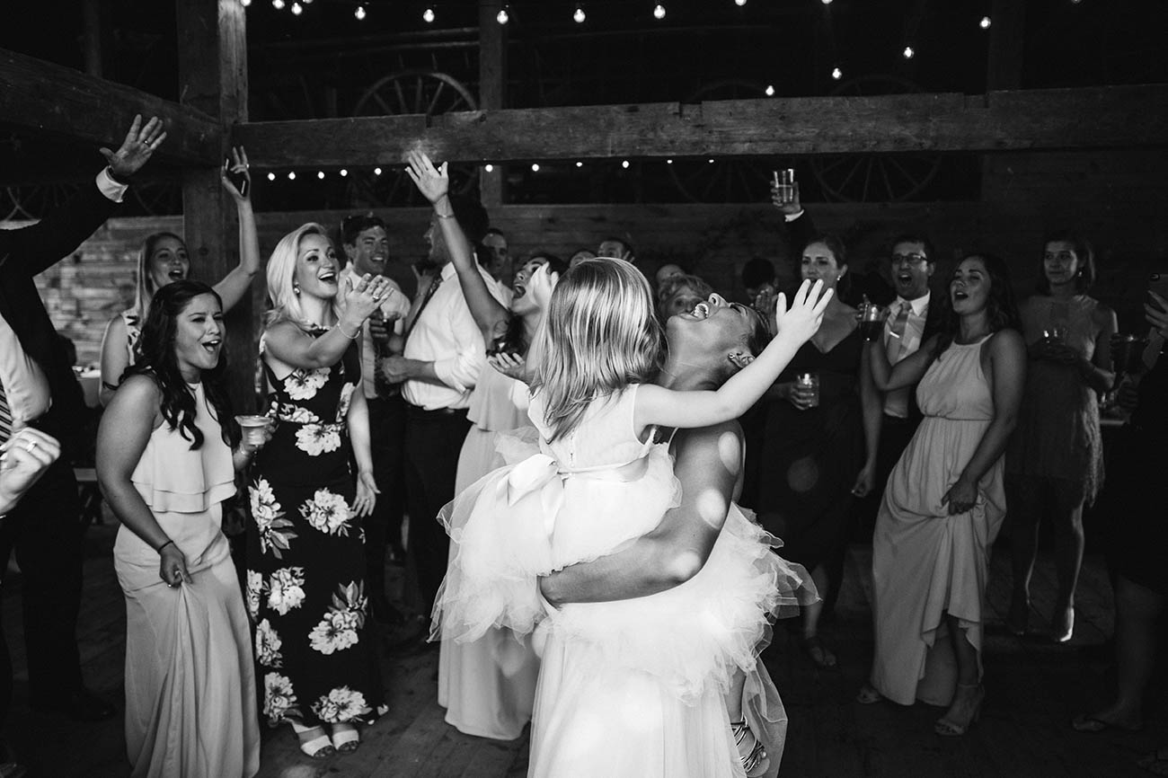 A documentary photograph of a bride dancing with the flower girl during their moody mountain farm wedding
