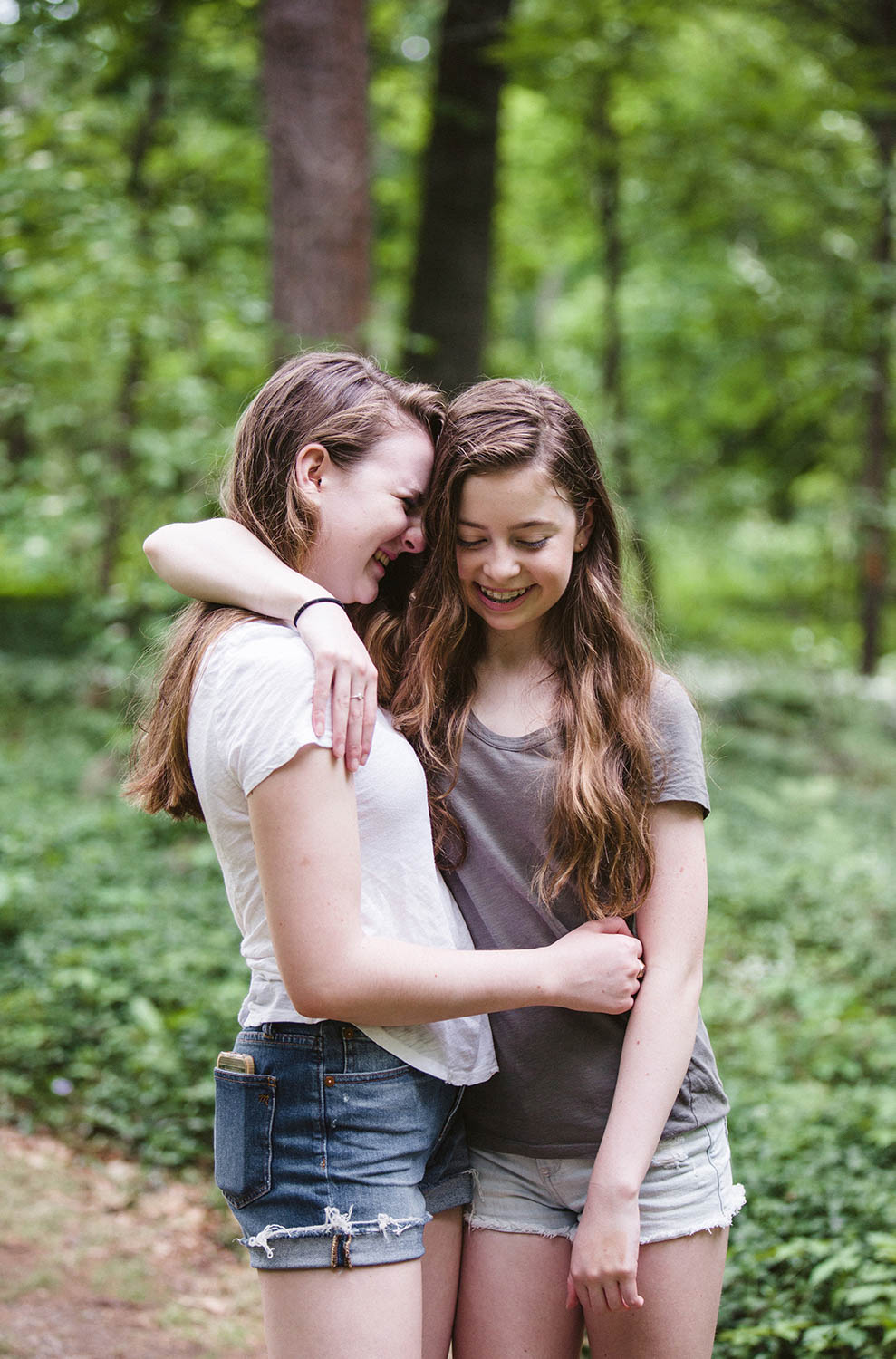 A documentary photograph of two sisters hugging and laughing during their Boston family session