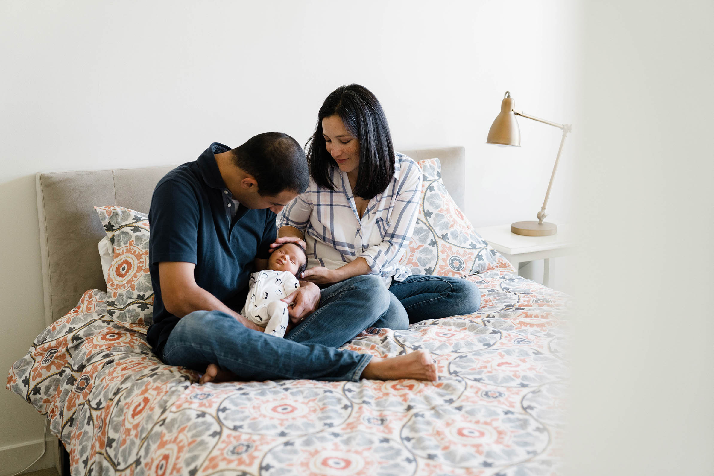 A documentary photograph of a family sitting on the bed with their newborn baby during an in home newborn session in Boston