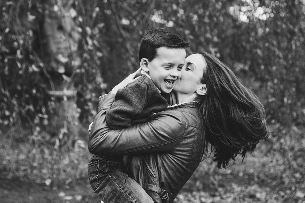 A documentary photograph of mom kissing her son during their family session at the Arnold Arboretum in Boston