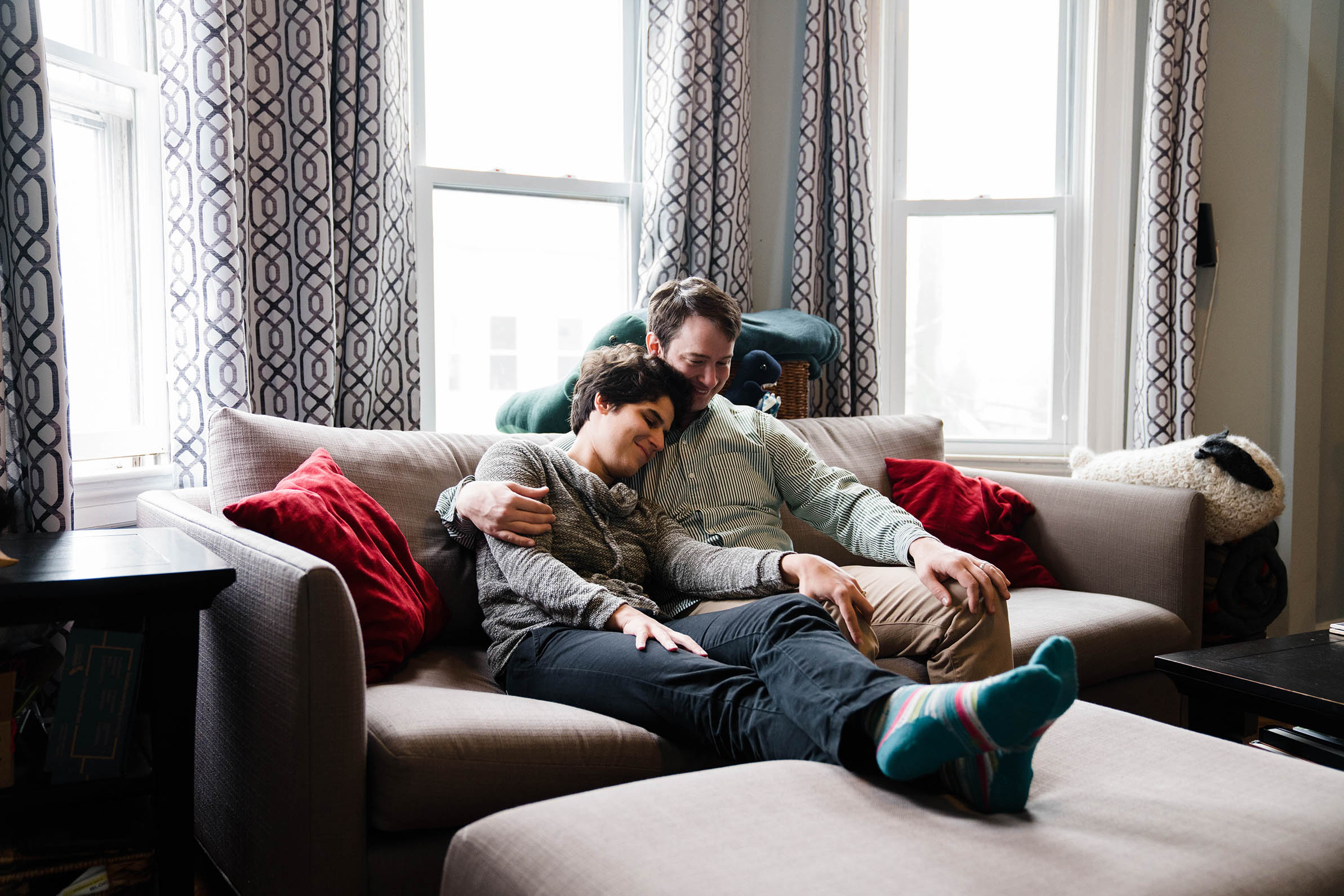 A documentary portrait of a couple cuddling on their couch at home during their Boston engagement session