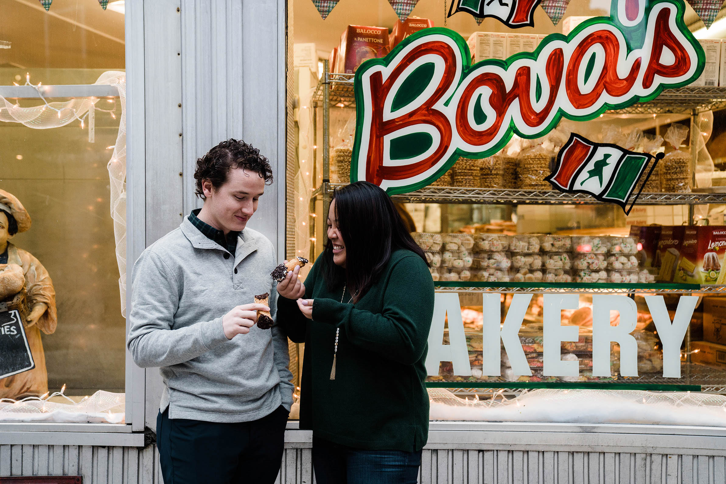 A documentary portrait of a couple eating a cannoli outside of Bova's Bakery in the North End during their Boston engagement session