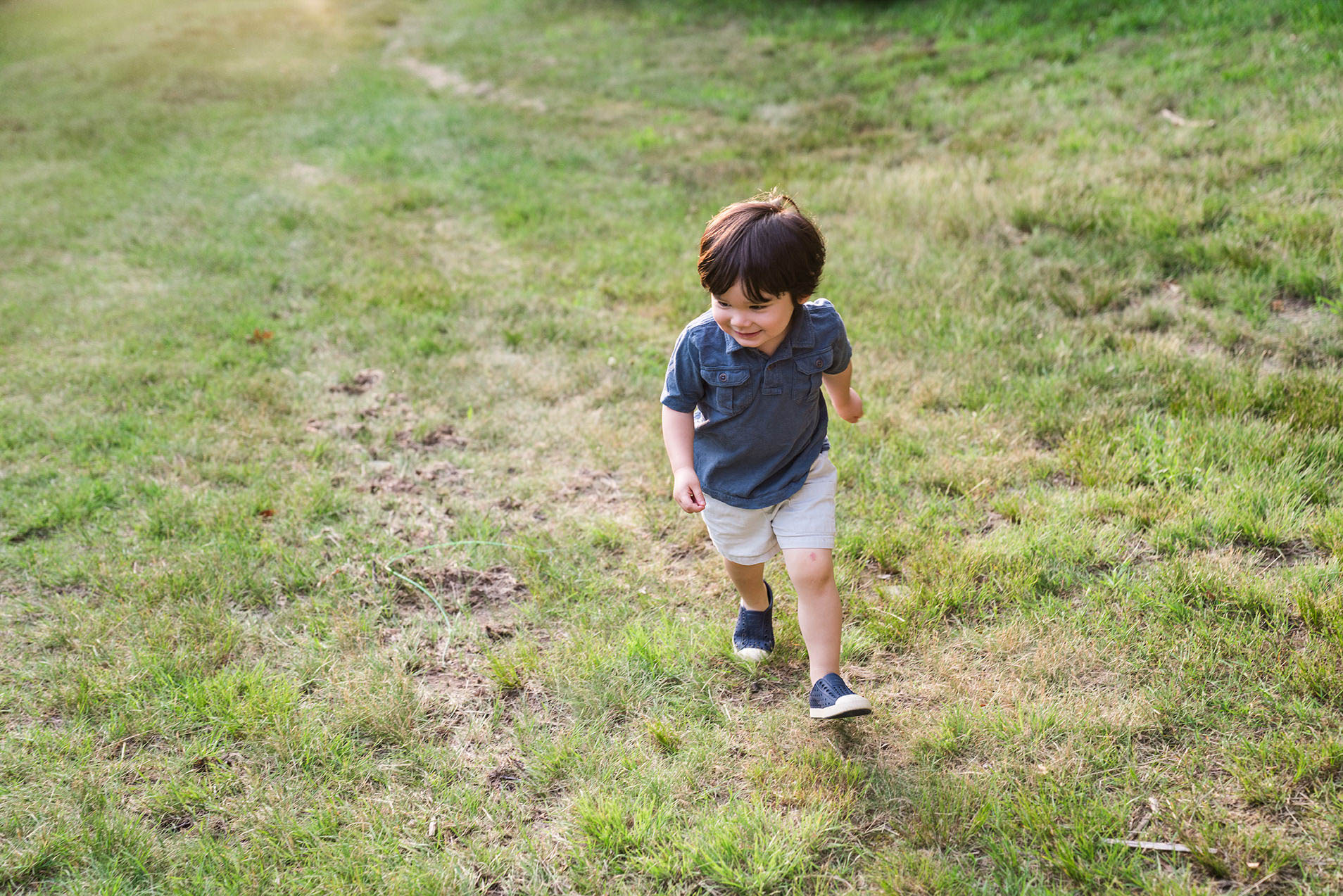 A documentary photograph of a boy running in the grass during a family session at Larz Anderson park in Boston