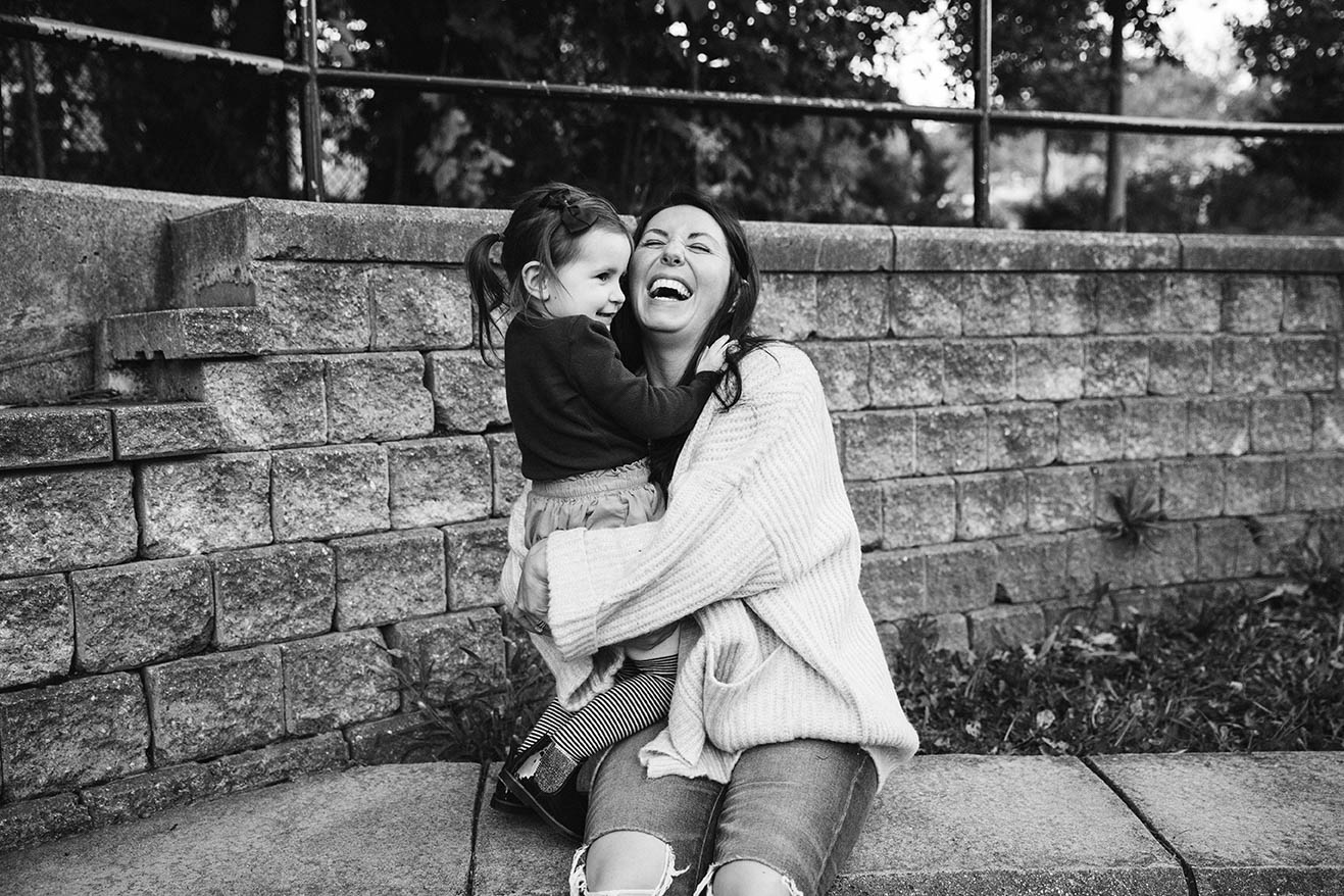 A documentary photograph of a mom and daughter laughing together at their local playground during an in home family life session in Boston's Jamaica Plain