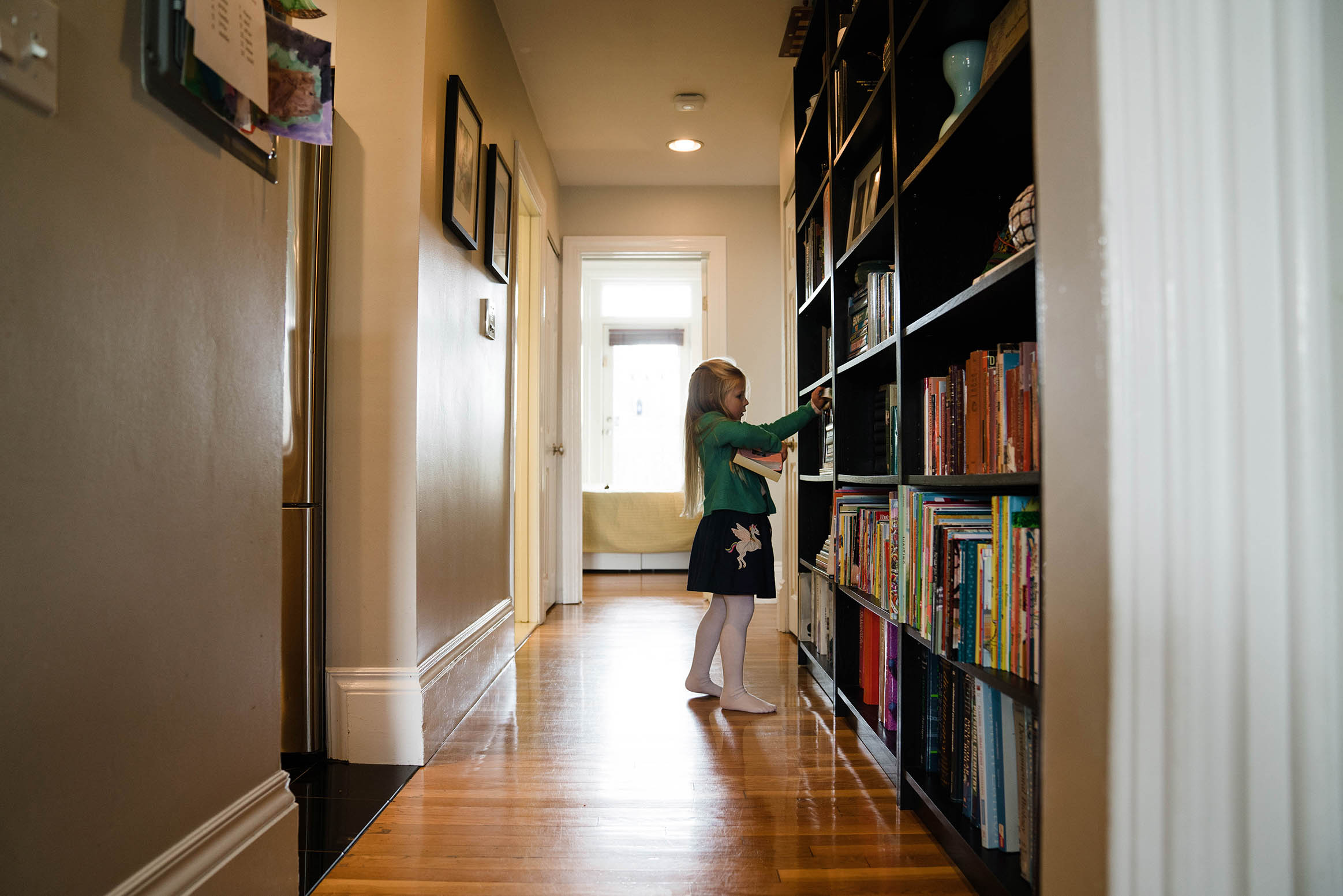A documentary photograph of a girl picking out a book to read during an in home family session in Boston's South End