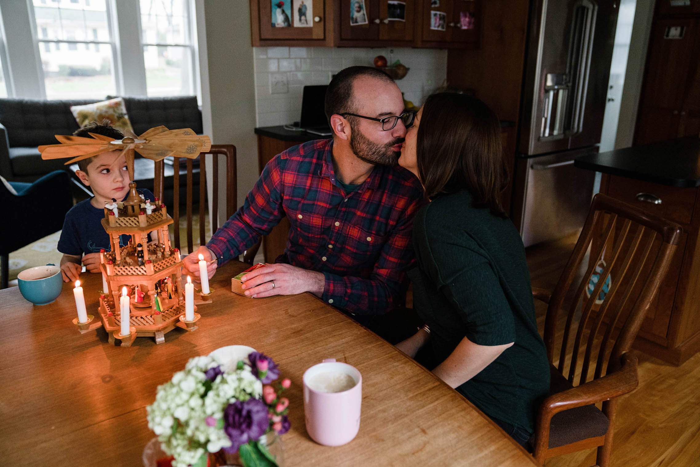 A documentary photograph of a parents kissing while they set up Christmas decorations during an in home family session in Boston