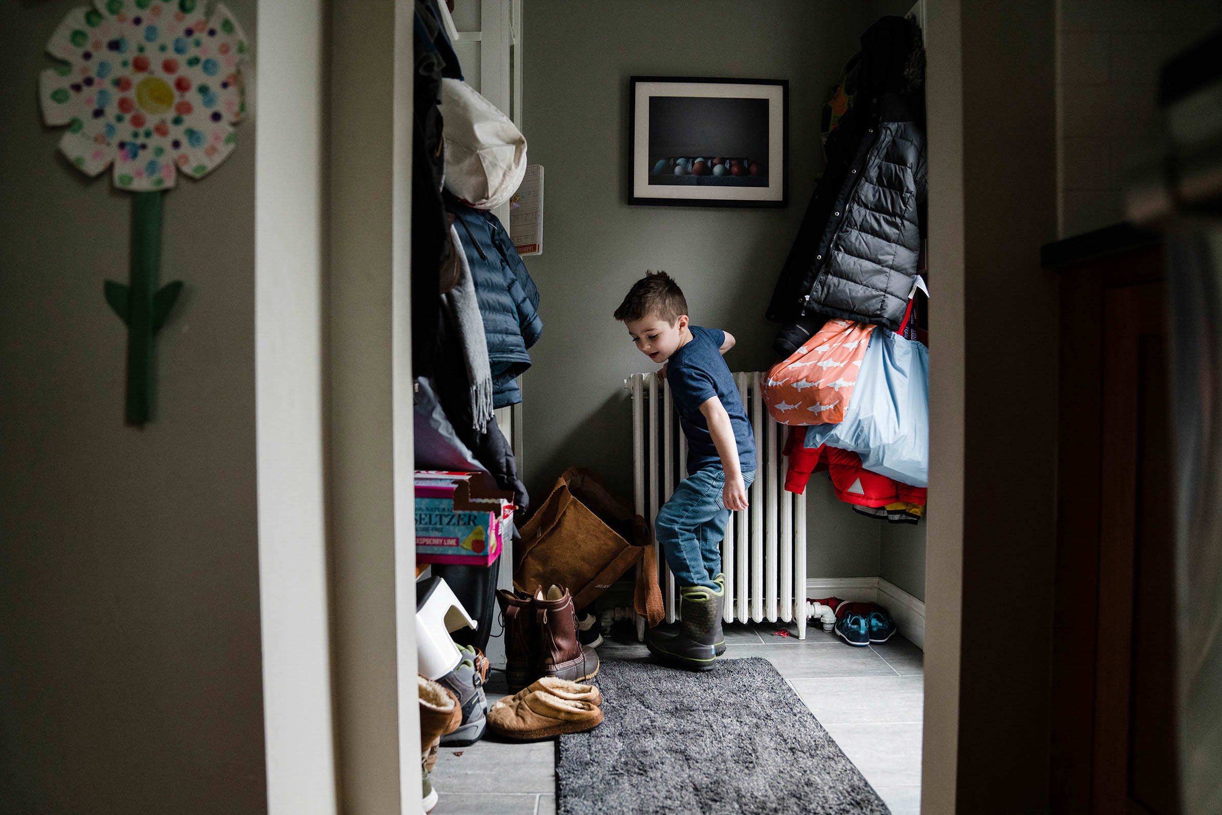 A documentary photograph of a boy putting on his boots before leaving the house during an in home family session in Boston