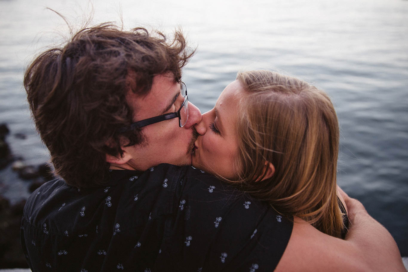 A documentary portrait of a couple kissing by the water during their Boston engagement session