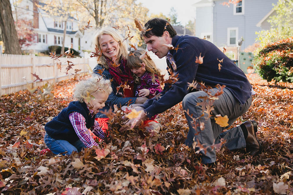A documentary photograph of a family playing in the leaves during an in home family session in Boston