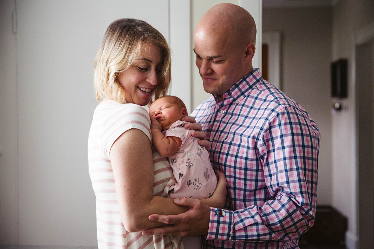 A documentary photograph of parents cuddling their newborn daughter during an in home family session in Boston