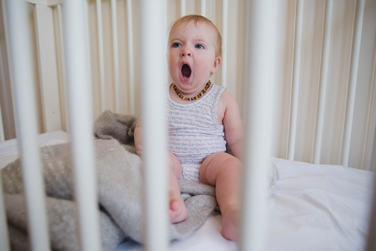 A documentary photograph of a baby yawning in her crib during an in home family session in Boston