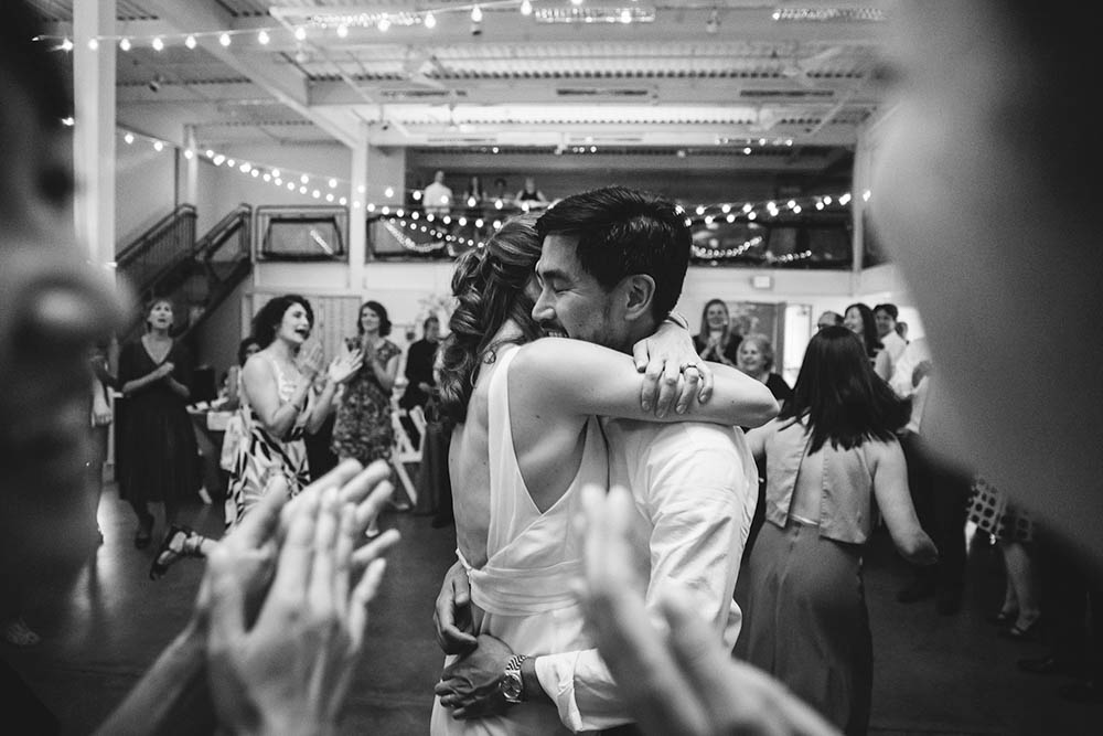 A documentary photograph of a bride and groom hugging on the dance floor during their Artists for Humanity wedding