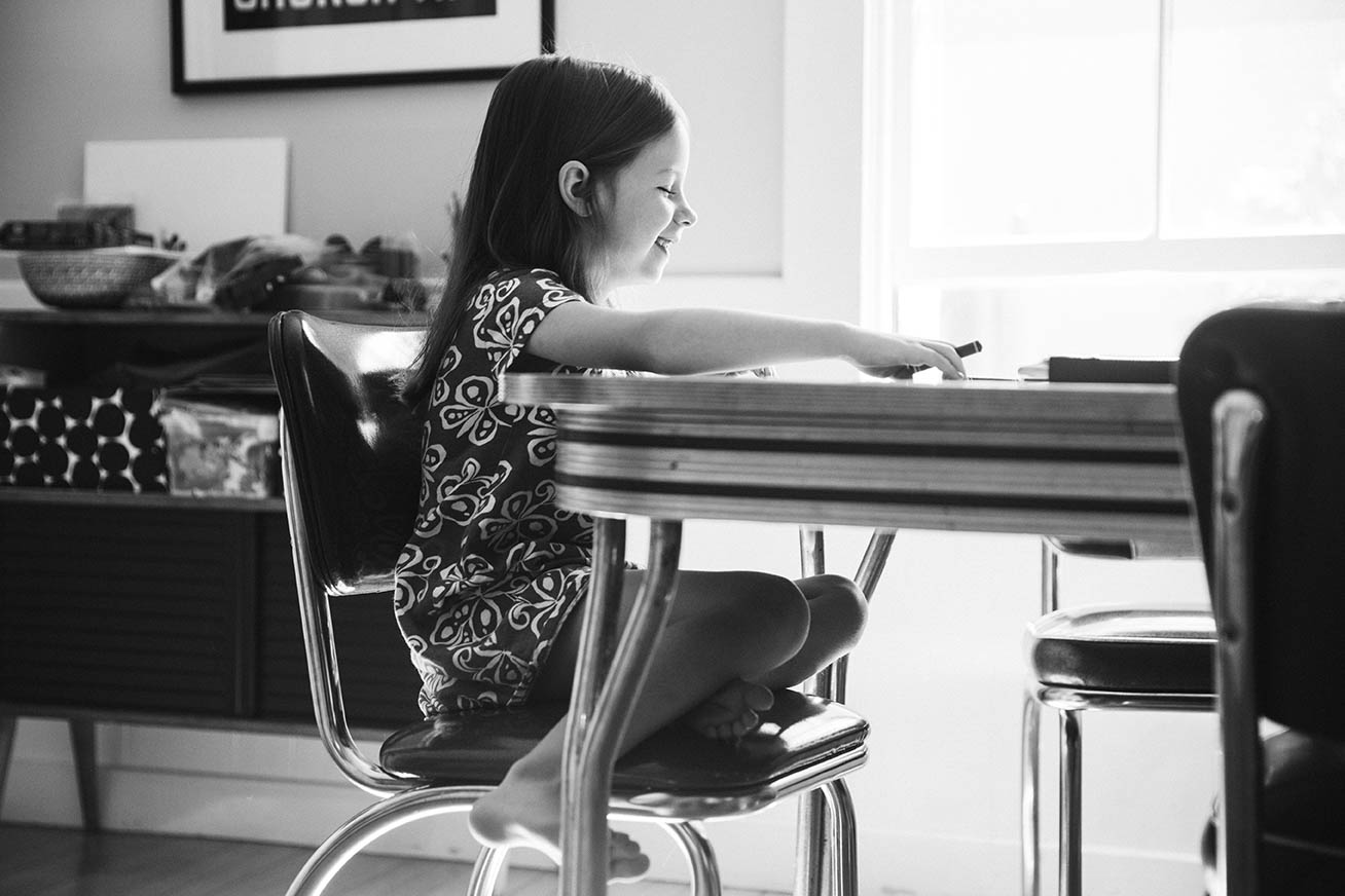 A documentary photograph of a girl laughing at the breakfast table during an in home family session in Boston