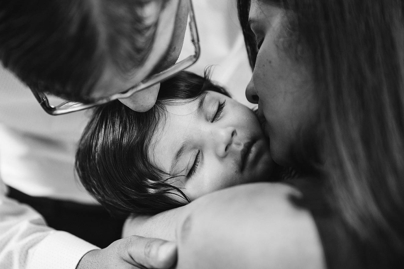 A documentary photograph of parents kissing their baby's head during an in home family session in Boston