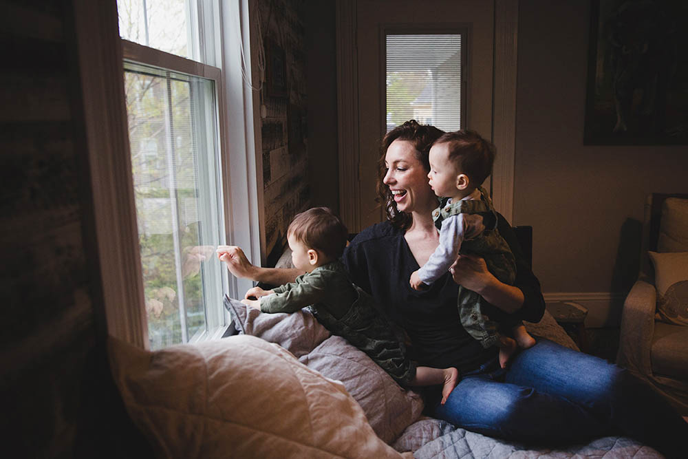 A documentary photograph of a mom looking out the window with her twin boys during an in home family session in Boston