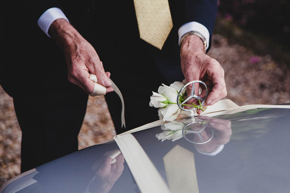 A documentary photograph of a grandfather adding a flower to the wedding car before a Boston wedding