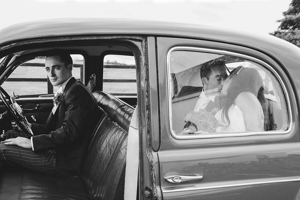 A documentary photograph of a bride and groom kissing in the back of a wedding car during their Boston wedding