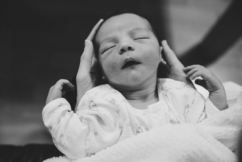 A documentary portrait of a newborn being held while sleeping during an in home family session in Boston