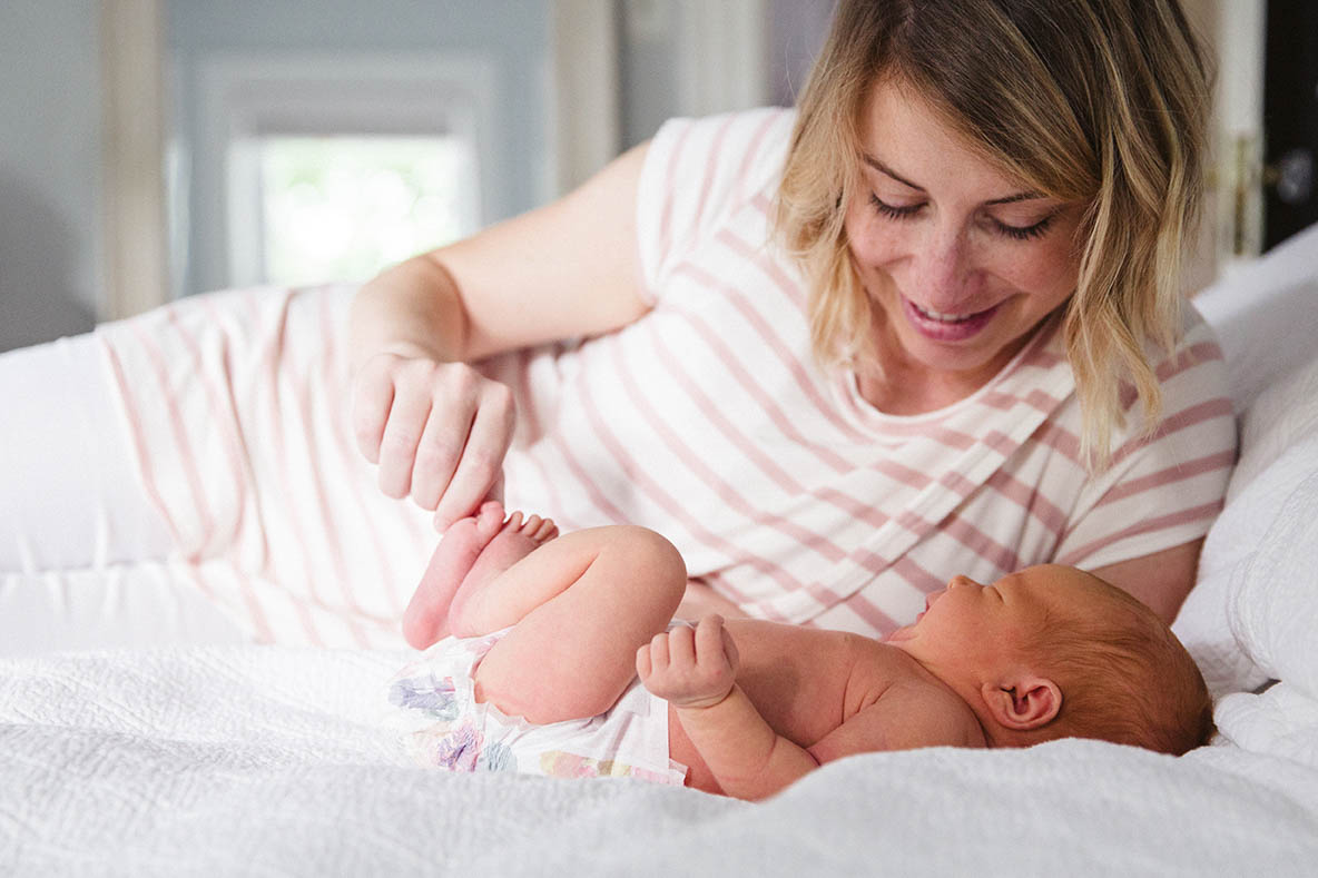 A documentary photograph of a mother with her newborn daughter in bed during an in home newborn session in Boston
