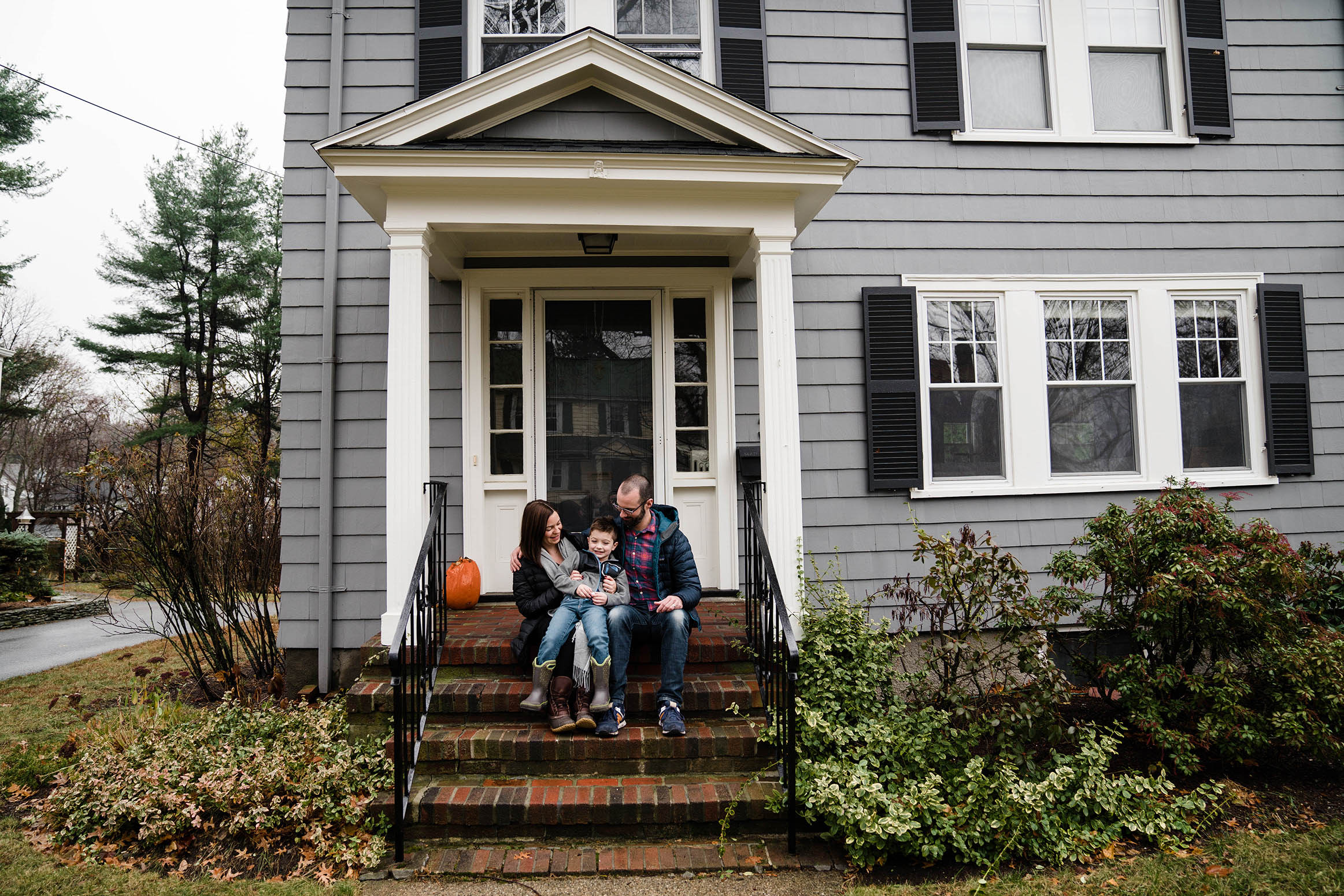 A documentary photograph of a family sitting on their porch together during an in home family session in Boston