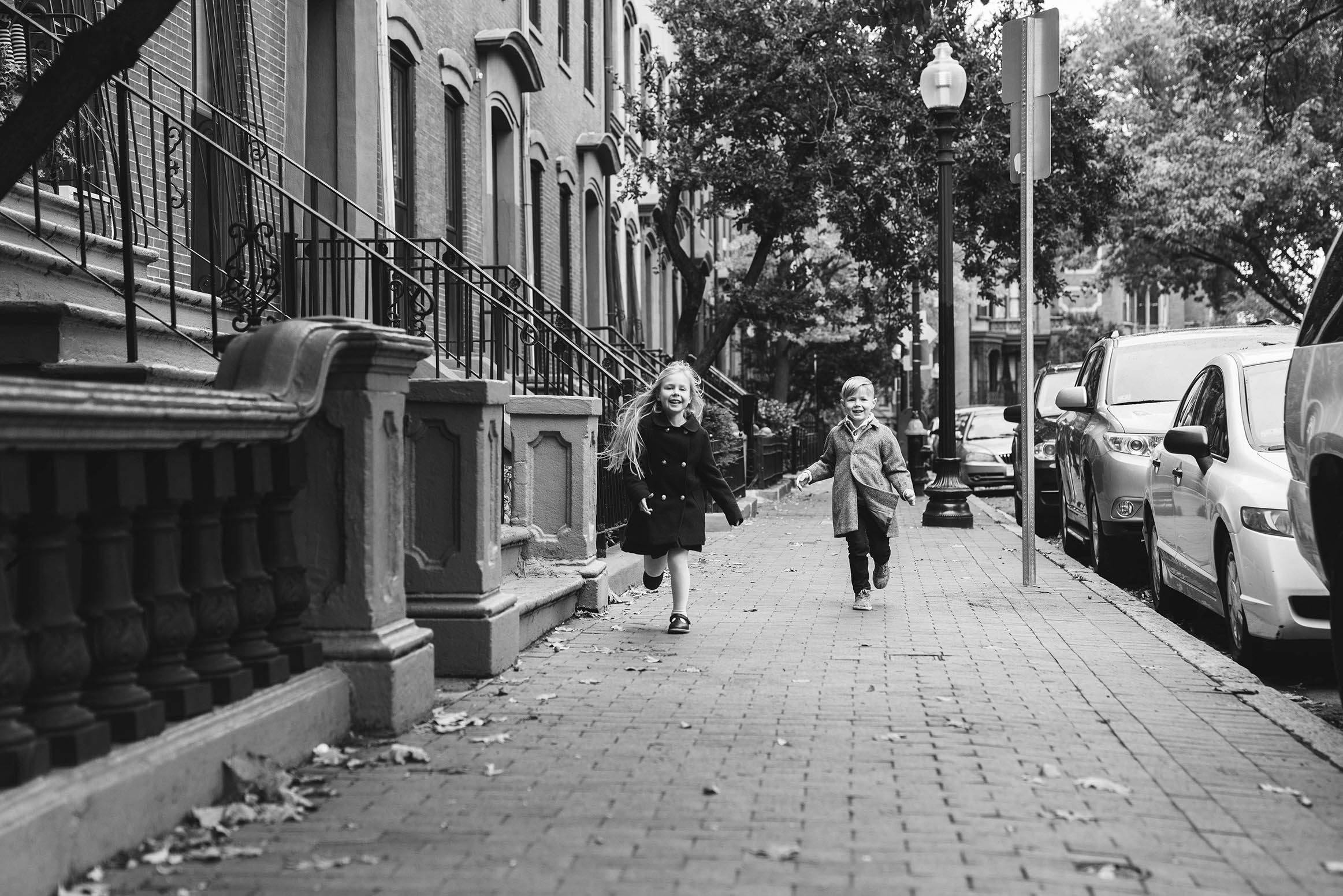 A documentary photograph of kids running on the sidewalk outside their home during an in home family session in Boston's South End