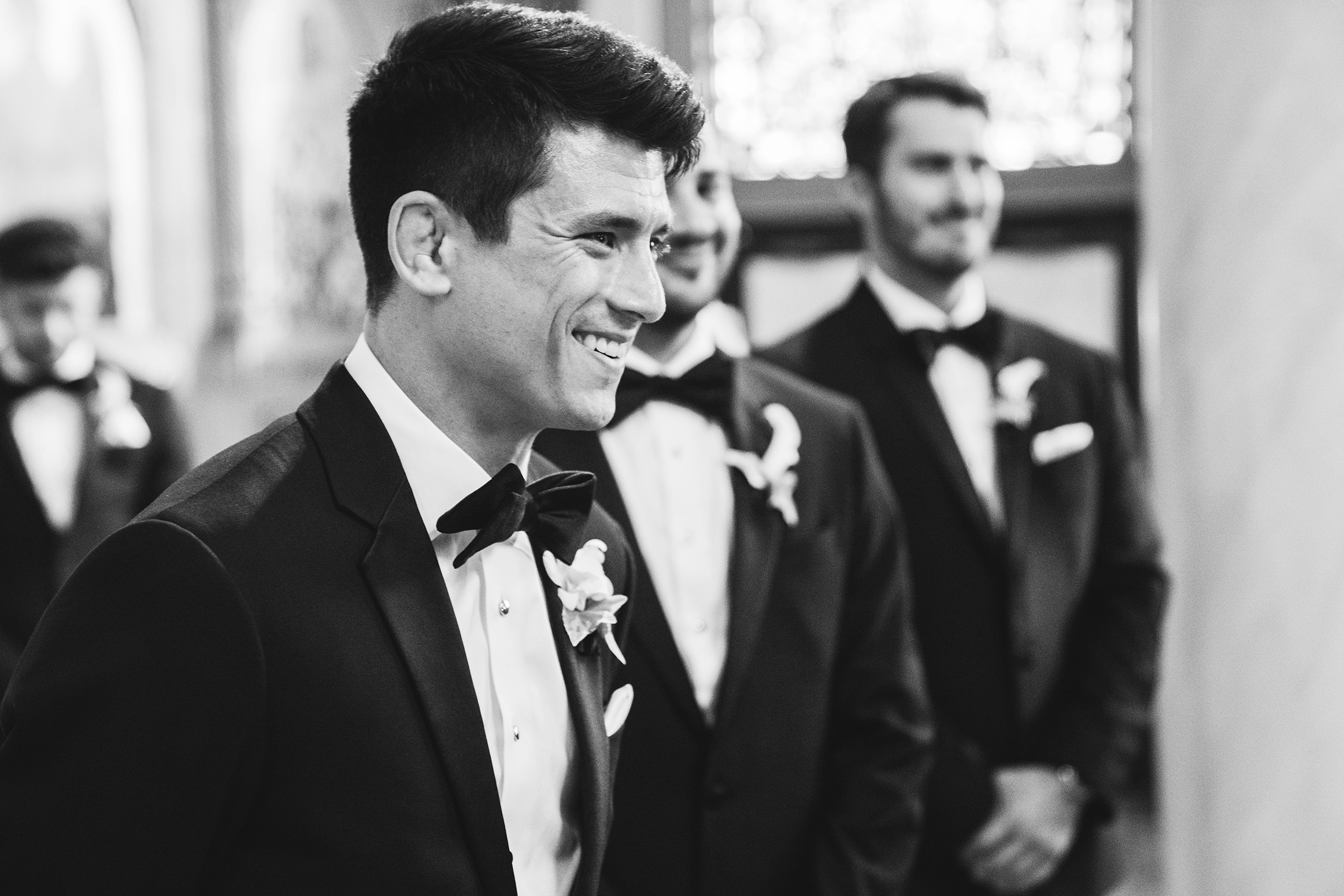 A documentary photograph featured in the best of wedding photography of 2019 showing a groom smiling as his bride walks up the aisle for their ceremony
