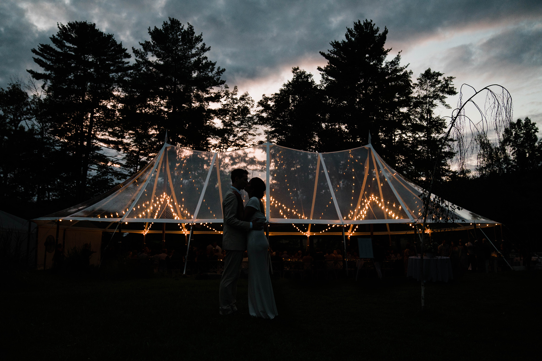 A documentary photograph featured in the best of wedding photography of 2019 showing a couple kissing outside the tent during their wedding reception