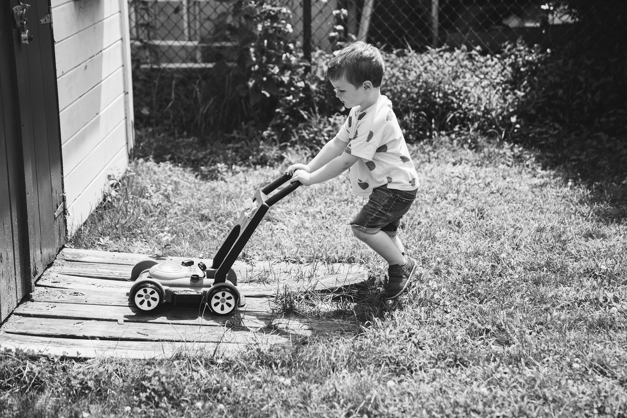 A documentary photograph of a boy mowing his lawn during an in home family session in Boston
