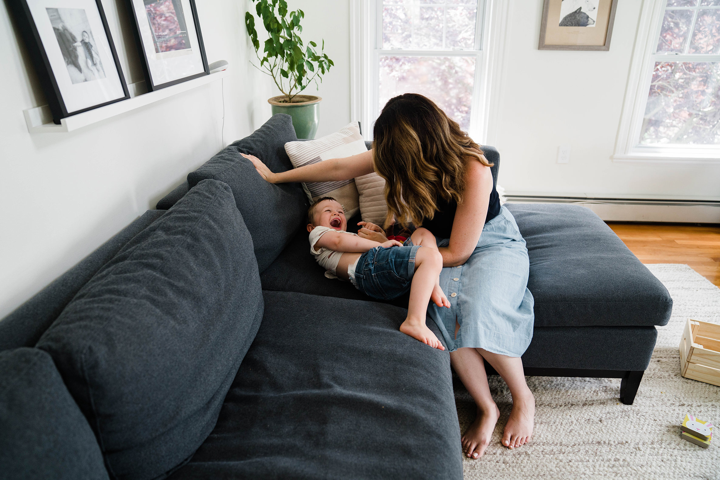 A documentary photograph of a mom playing with her son on the couch during an in home family session in Boston. 