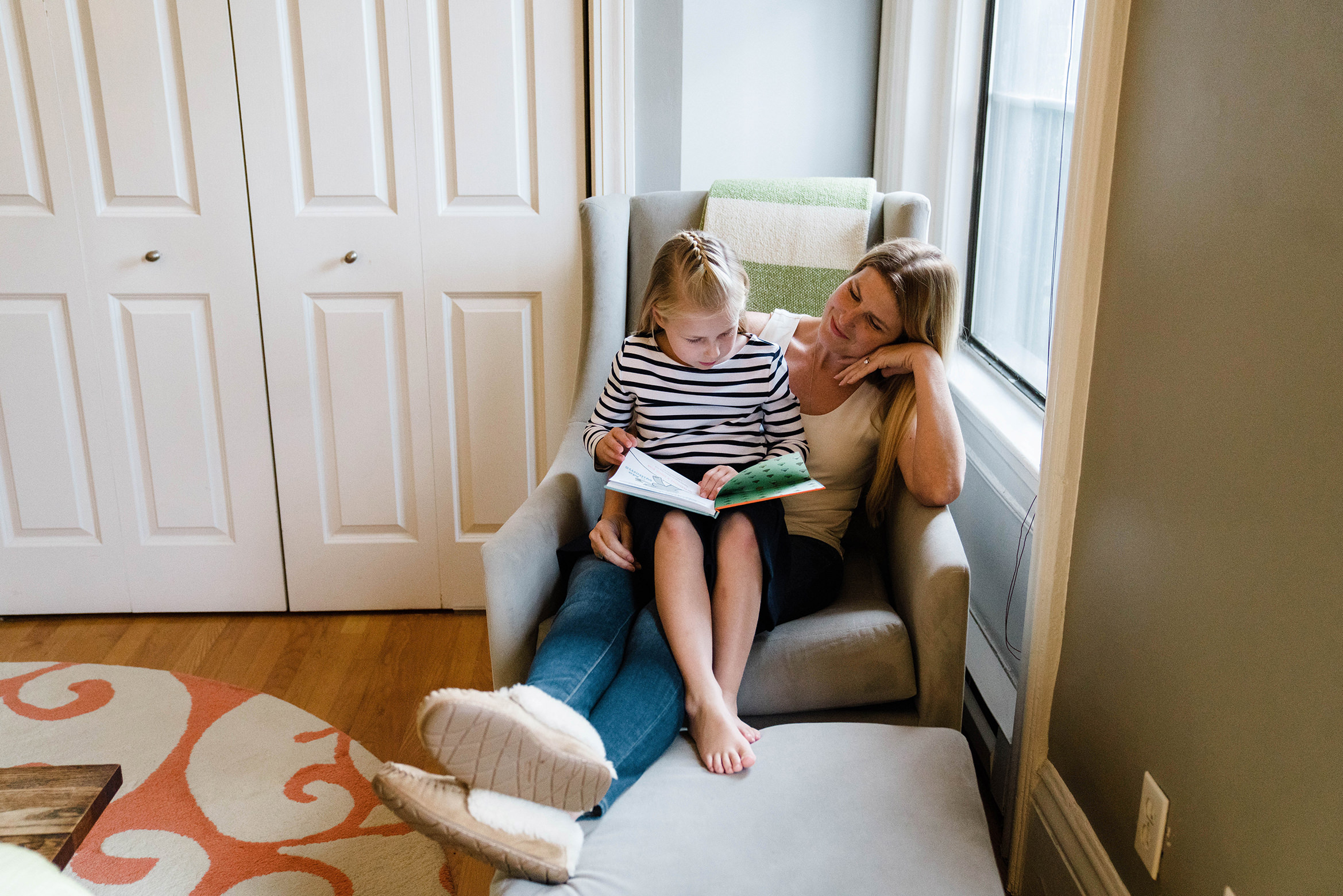 A documentary photograph of mom and daughter reading a book together during an in home family session in Boston